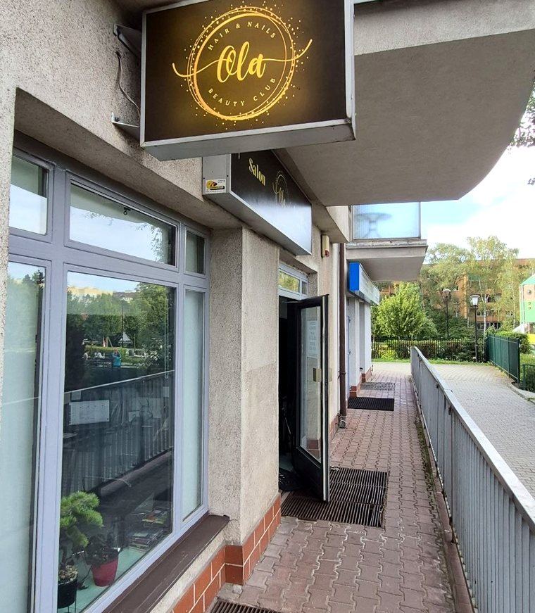 Wejście do salonu Ola Beauty Club przy ul. Kobierzyńskiej 63 w Krakowie — podświetlony szyld nad przeszklonymi drzwiami